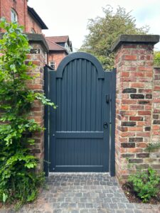 Link to our range of garden gates showing a grey painted bespoke garden gate fitted to hardwood battens between brick piers with a coded lock.