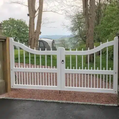 Link to our range of Wooden Driveway gates. Showing a white spindle white painted wooden gate between two stone piers.